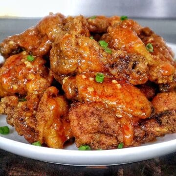 Crispy buffalo chicken wings tossed in a homemade buffalo sauce and garnished with green onions on a white plate.