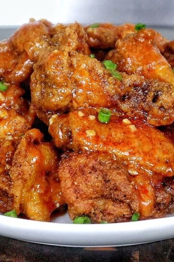 Crispy buffalo chicken wings tossed in a homemade buffalo sauce and garnished with green onions on a white plate.