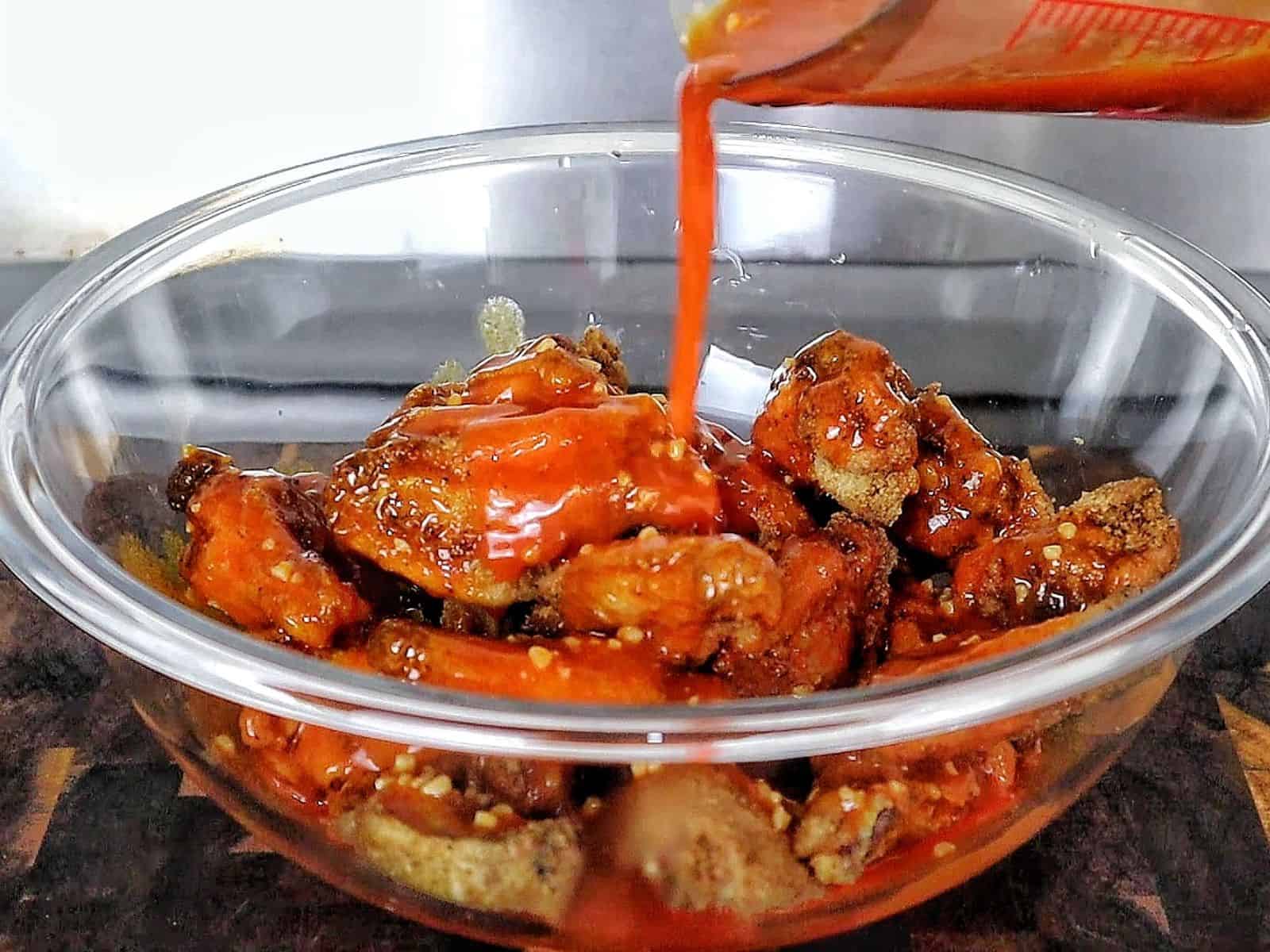 Crispy buffalo chicken wings tossed in a homemade buffalo sauce and garnished with green onions on a white plate.