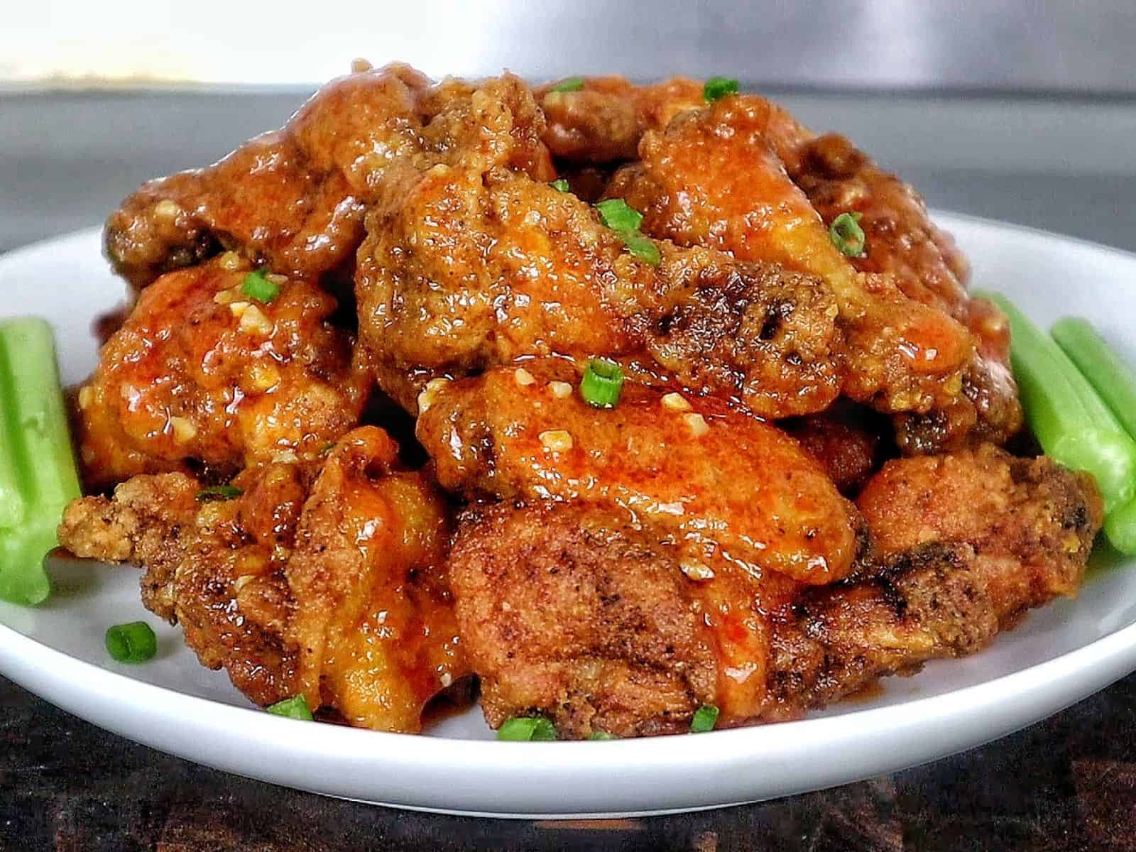 Crispy buffalo chicken wings tossed in a homemade buffalo sauce and garnished with green onions on a white plate.