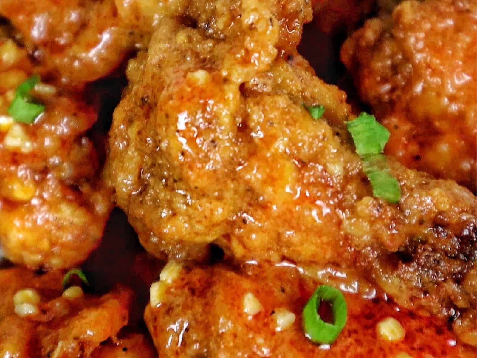 Crispy buffalo chicken wings tossed in a homemade buffalo sauce and garnished with green onions on a white plate.