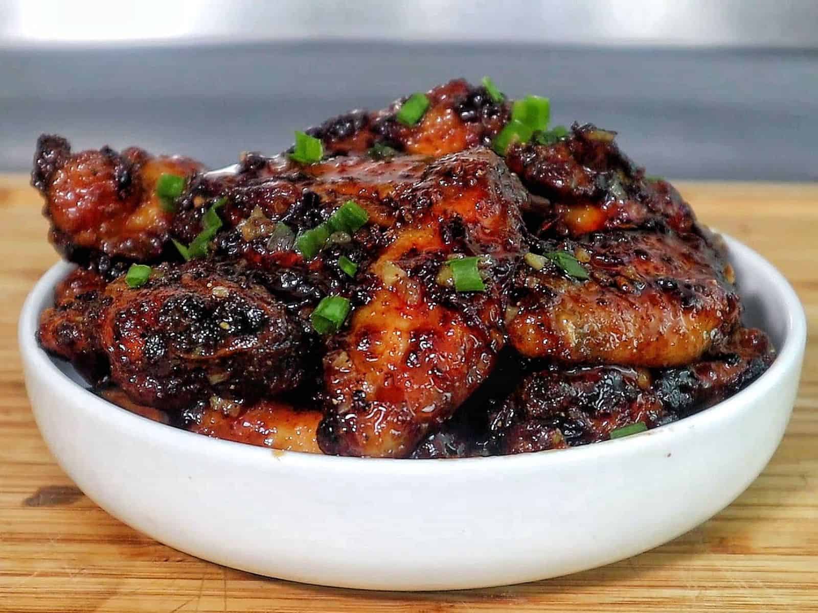 Air fryer honey chipotle chicken wings coated in a sticky sauce, garnished with chopped green onions.