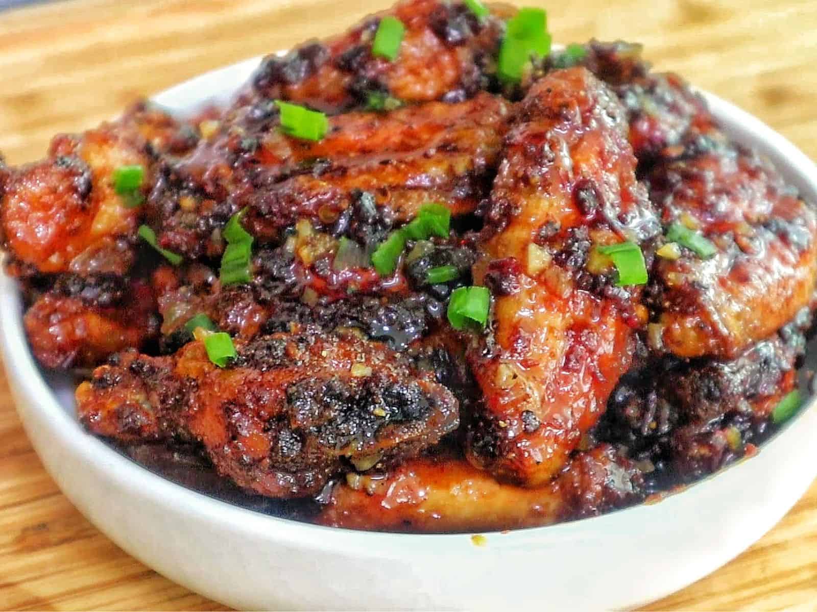 Air fryer honey chipotle chicken wings coated in a sticky sauce, garnished with chopped green onions.