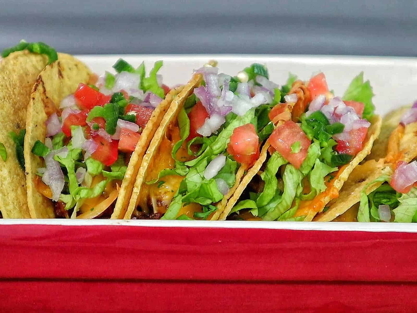 Cheesy oven baked tacos filled with seasoned ground beef, melted cheddar and smoked gouda cheese, topped with lettuce, tomatoes, onions, and sour cream in crispy taco shells.