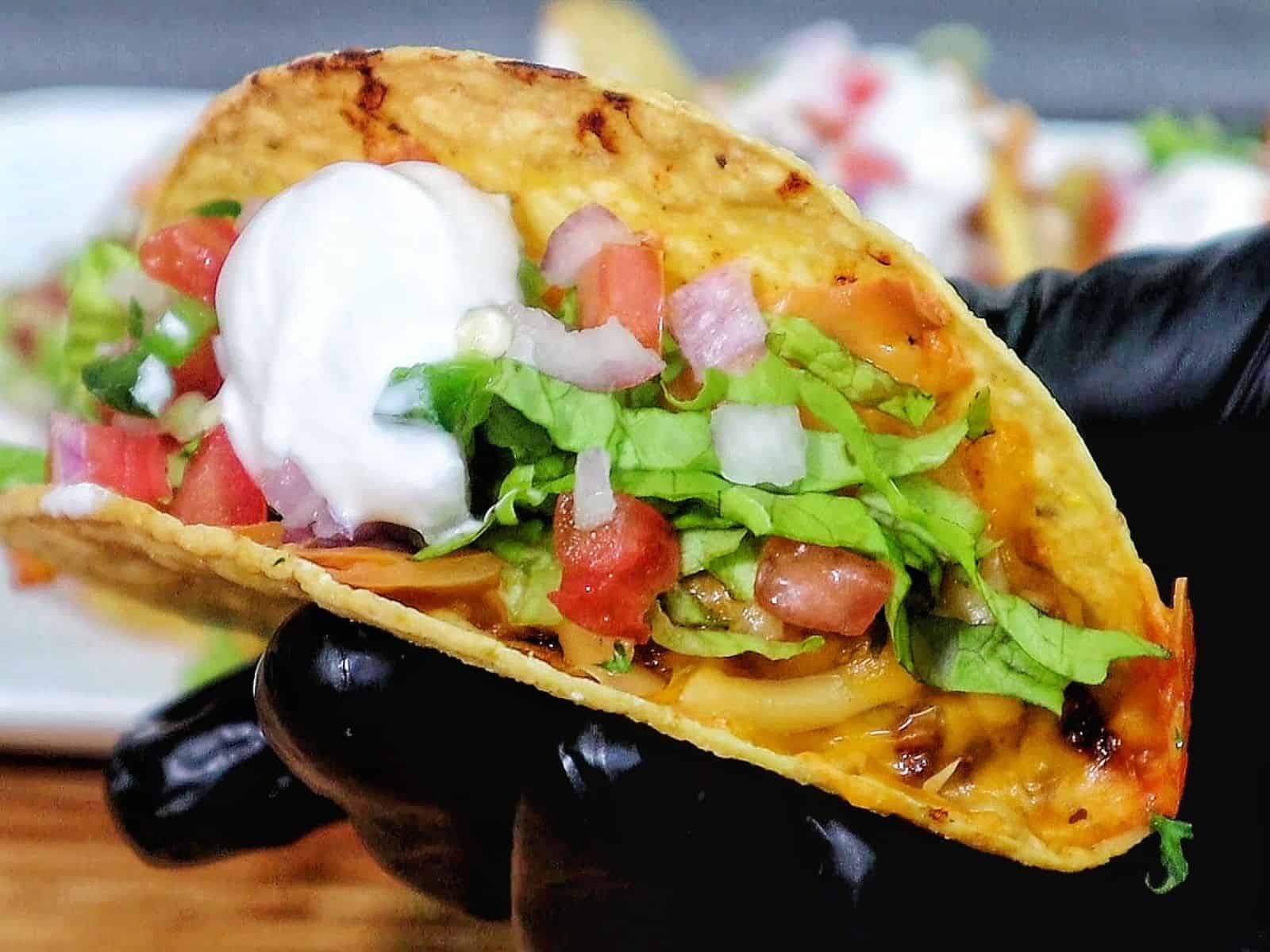 Cheesy oven baked tacos filled with seasoned ground beef, melted cheddar and smoked gouda cheese, topped with lettuce, tomatoes, onions, and sour cream in crispy taco shells.