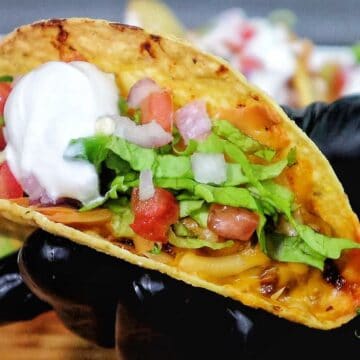 Cheesy oven baked tacos filled with seasoned ground beef, melted cheddar and smoked gouda cheese, topped with lettuce, tomatoes, onions, and sour cream in crispy taco shells.