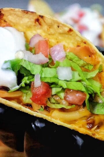 Cheesy oven baked tacos filled with seasoned ground beef, melted cheddar and smoked gouda cheese, topped with lettuce, tomatoes, onions, and sour cream in crispy taco shells.