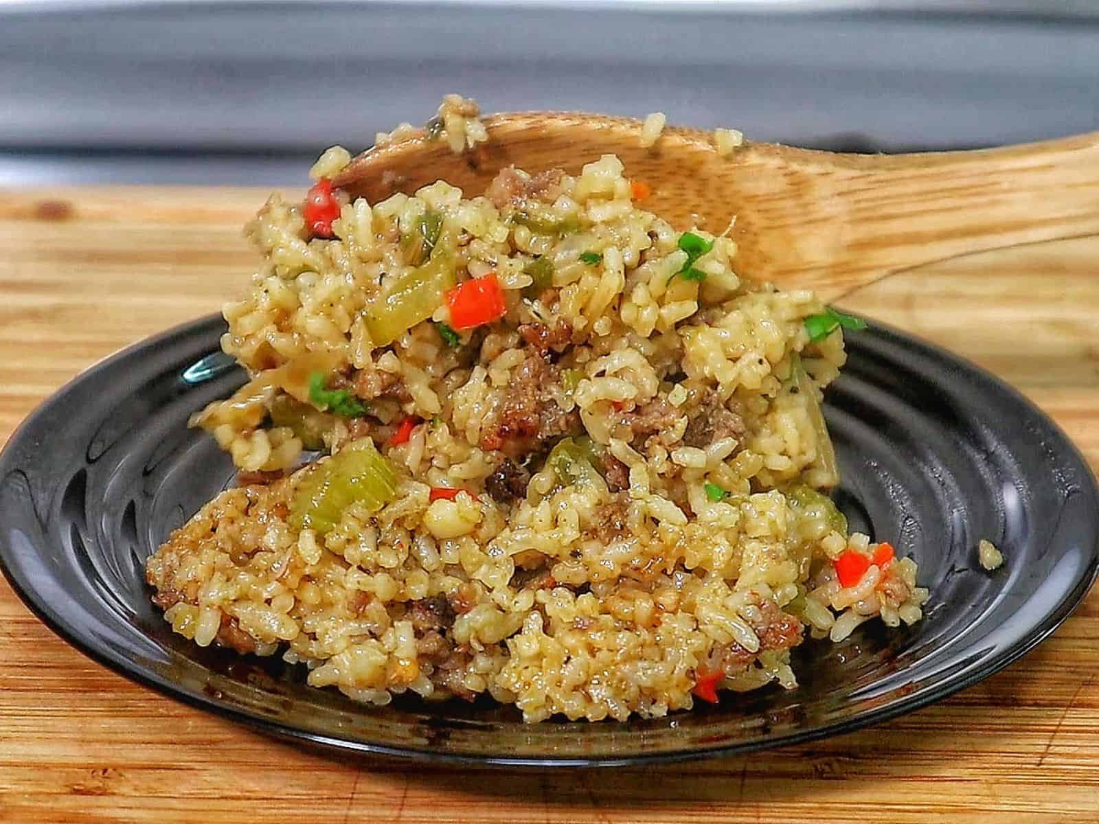Pappadeaux dirty rice made with seasoned sausage, fluffy long-grain rice, diced bell peppers, celery, and onions, cooked in a cast iron skillet and garnished with fresh parsley.