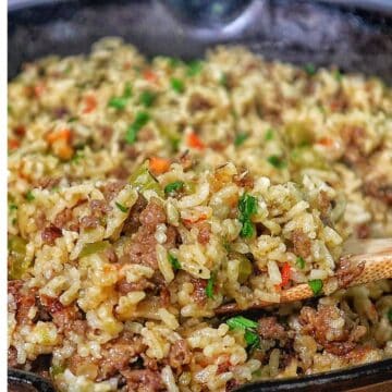 Pappadeaux dirty rice made with seasoned sausage, fluffy long-grain rice, diced bell peppers, celery, and onions, cooked in a cast iron skillet and garnished with fresh parsley.