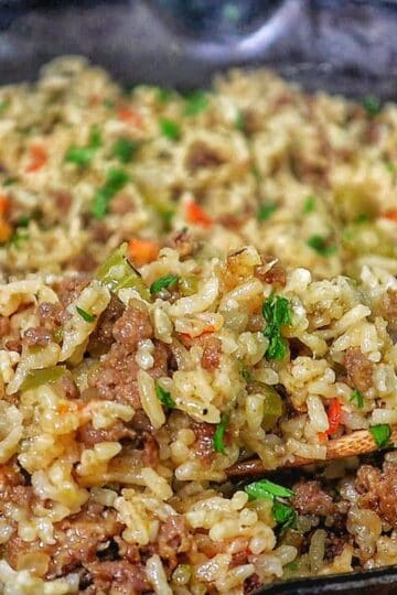 Pappadeaux dirty rice made with seasoned sausage, fluffy long-grain rice, diced bell peppers, celery, and onions, cooked in a cast iron skillet and garnished with fresh parsley.