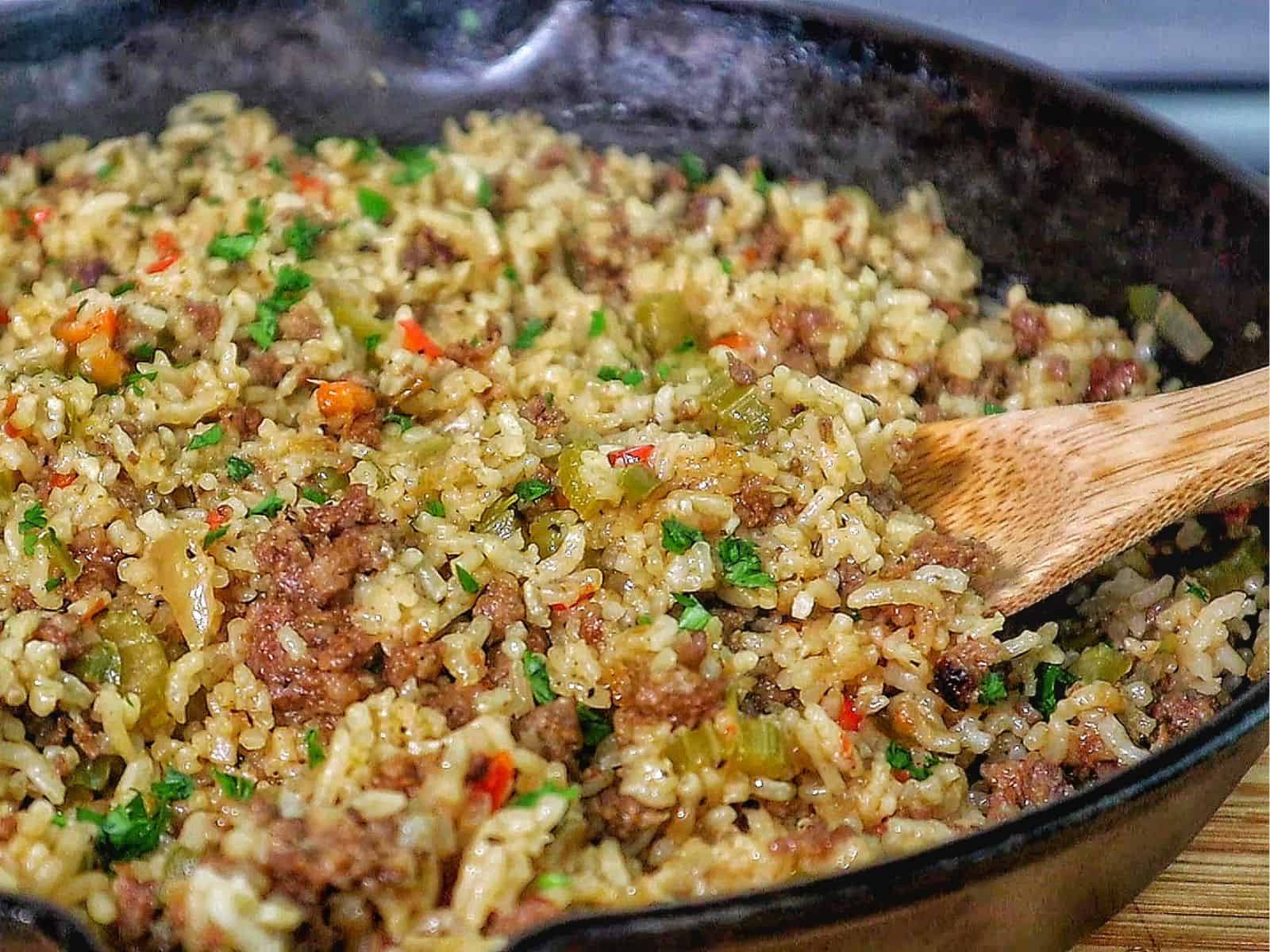 Pappadeaux dirty rice made with seasoned sausage, fluffy long-grain rice, diced bell peppers, celery, and onions, cooked in a cast iron skillet and garnished with fresh parsley.