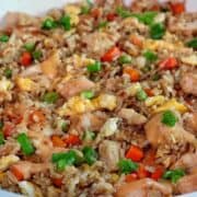 A plate of bang bang fried rice topped with green onions, featuring diced chicken, scrambled eggs, peas, carrots, and creamy sweet chili sauce drizzled throughout.