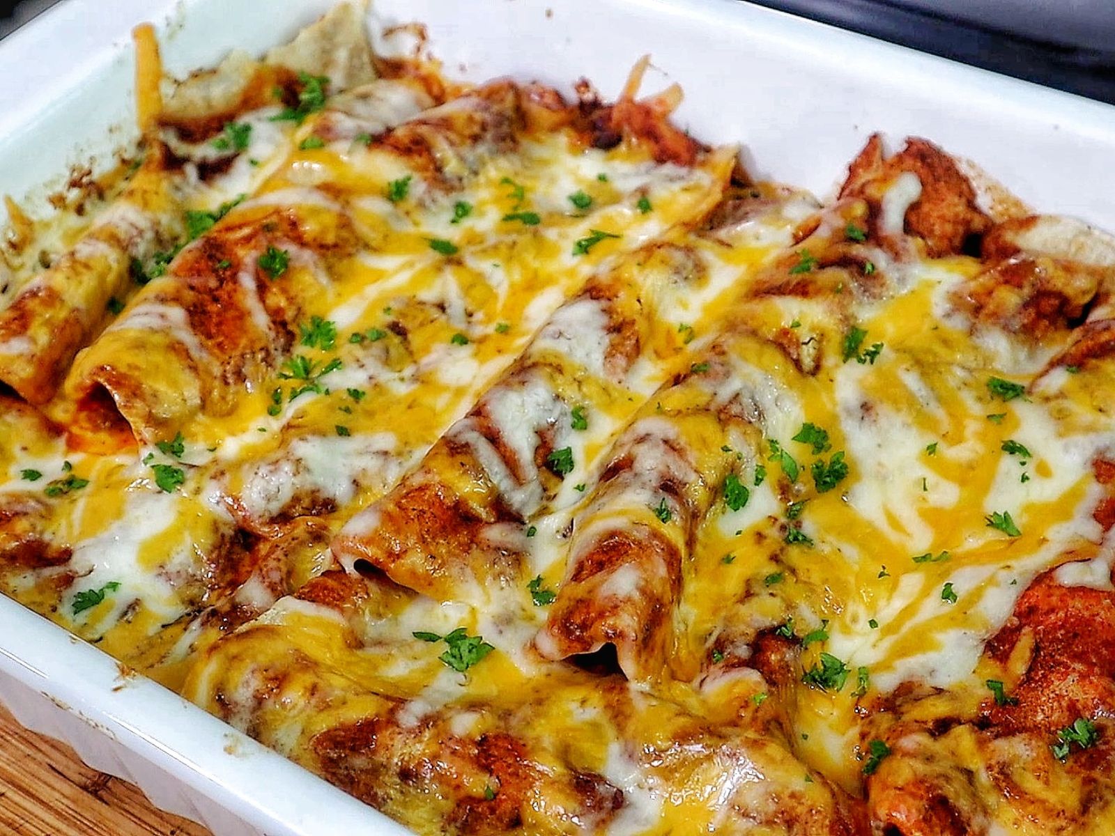 cheesy beef enchiladas in a white baking dish topped with melted cheddar and Monterey Jack cheese, garnished with fresh parsley