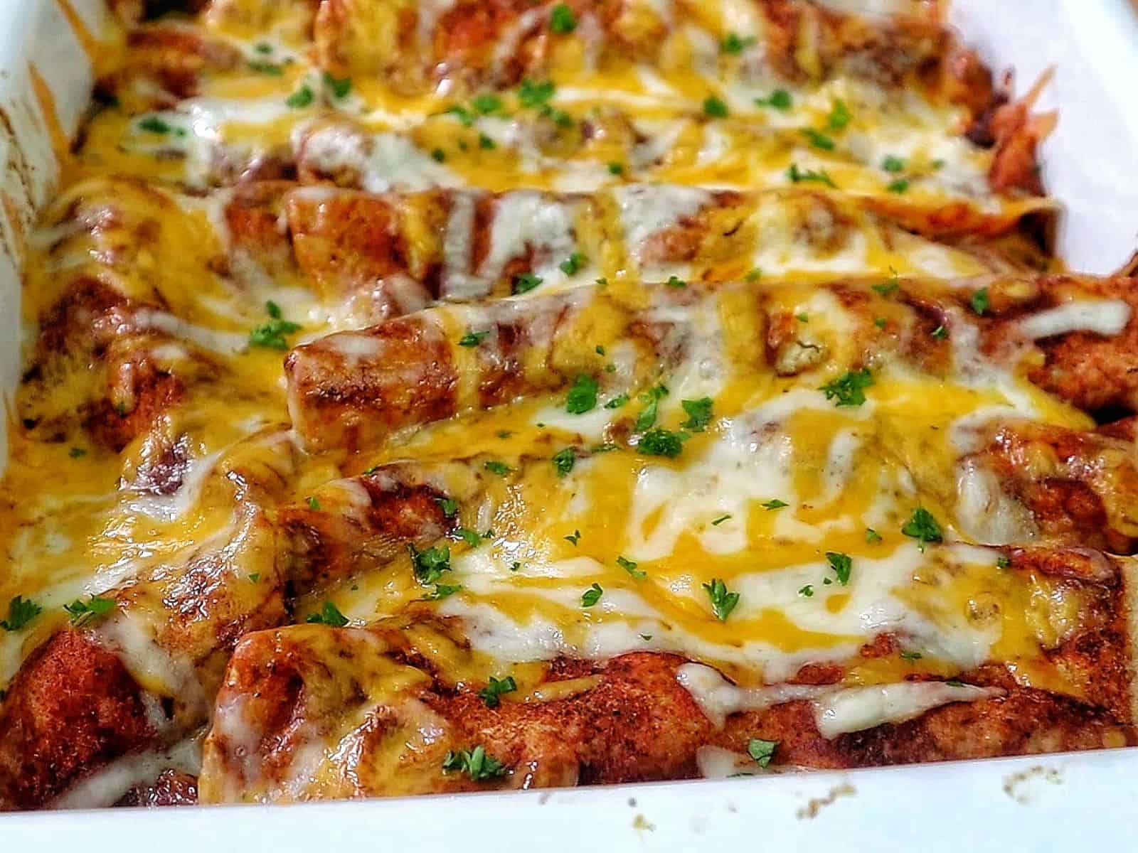 cheesy beef enchiladas in a white baking dish topped with melted cheddar and Monterey Jack cheese, garnished with fresh parsley