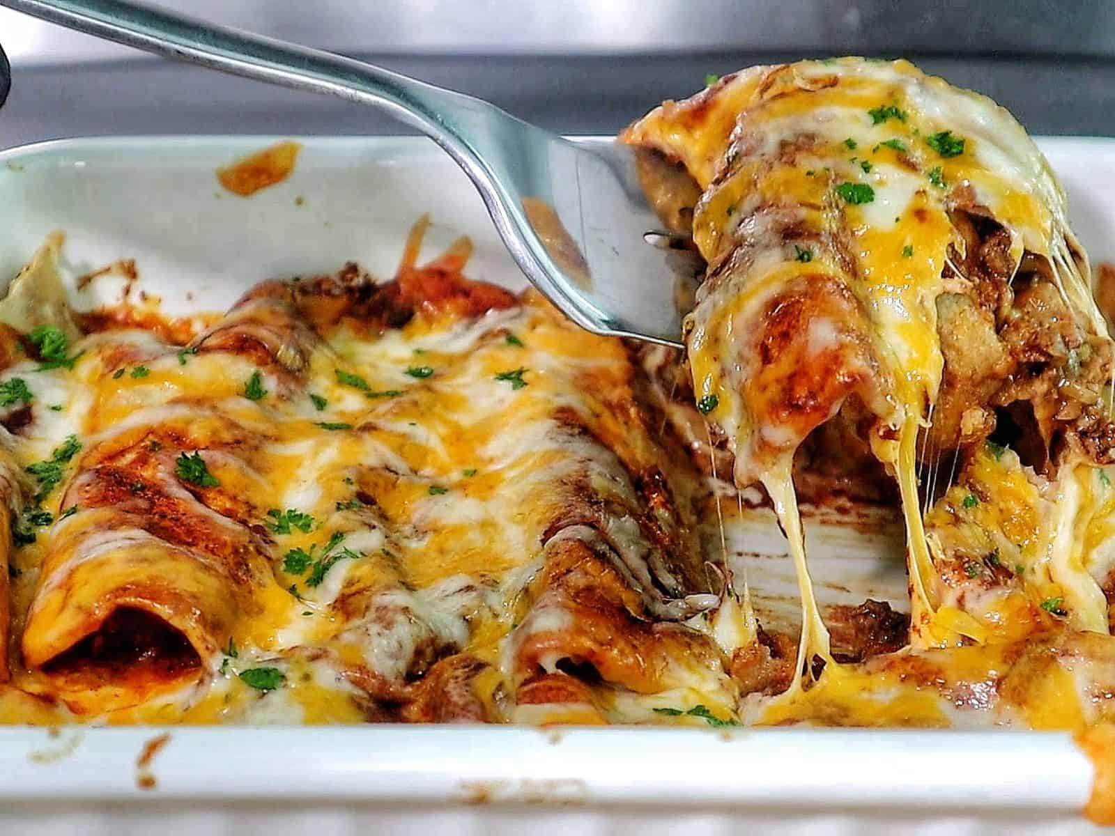 cheesy beef enchiladas in a white baking dish topped with melted cheddar and Monterey Jack cheese, garnished with fresh parsley