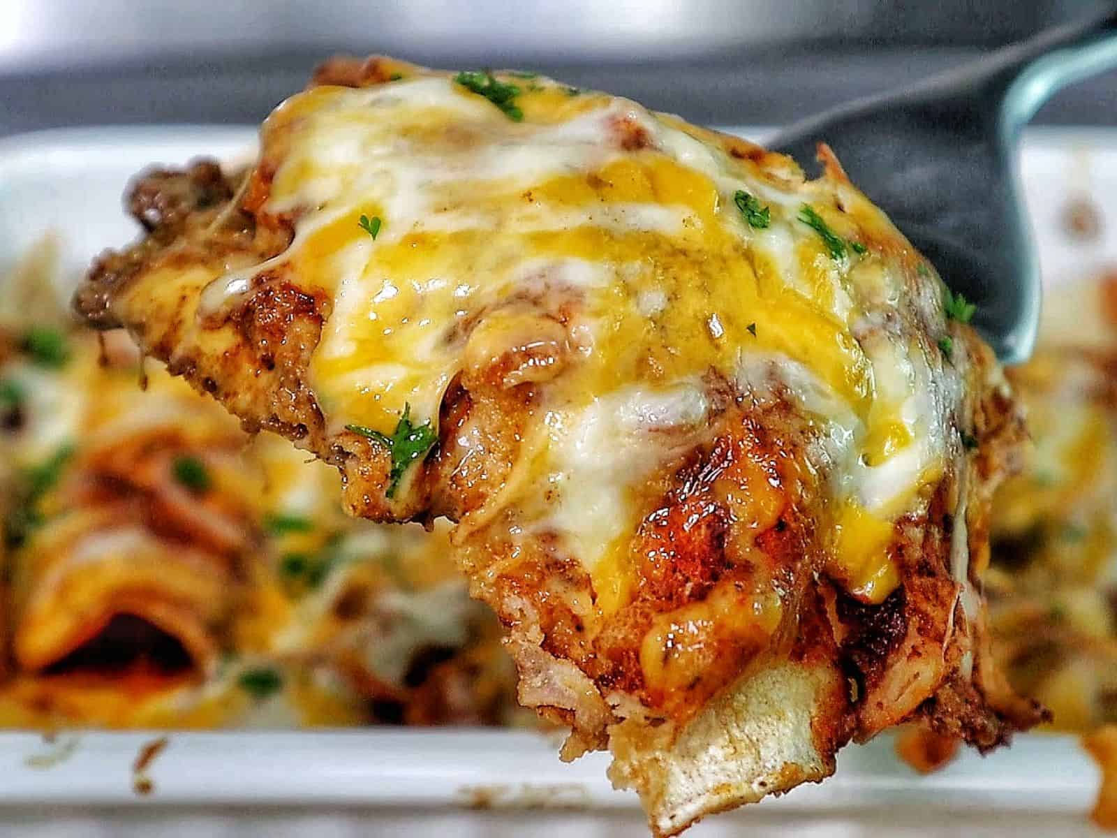 cheesy beef enchiladas in a white baking dish topped with melted cheddar and Monterey Jack cheese, garnished with fresh parsley