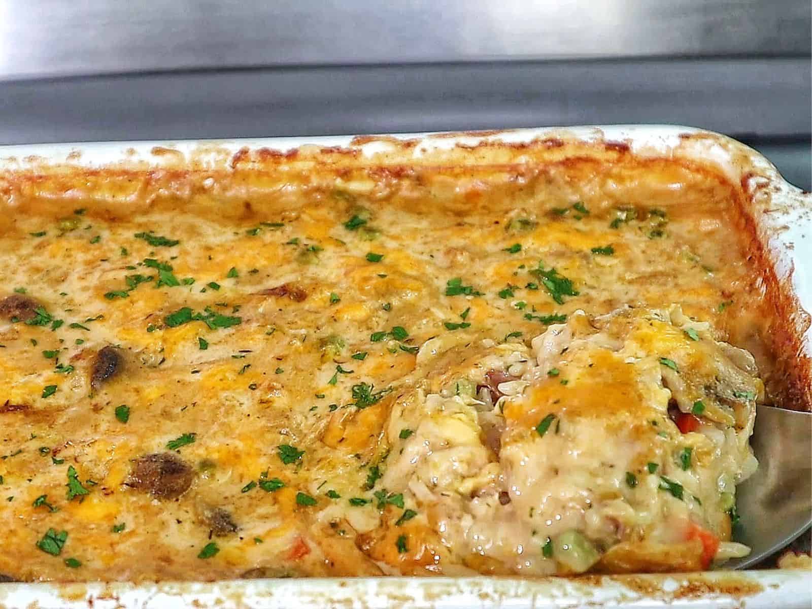 Creamy chicken and rice casserole topped with melted cheddar cheese, peas, carrots, and mushrooms with fresh parsley garnish.