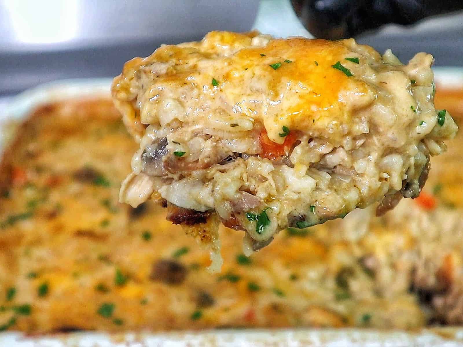 Creamy chicken and rice casserole topped with melted cheddar cheese, peas, carrots, and mushrooms with fresh parsley garnish.