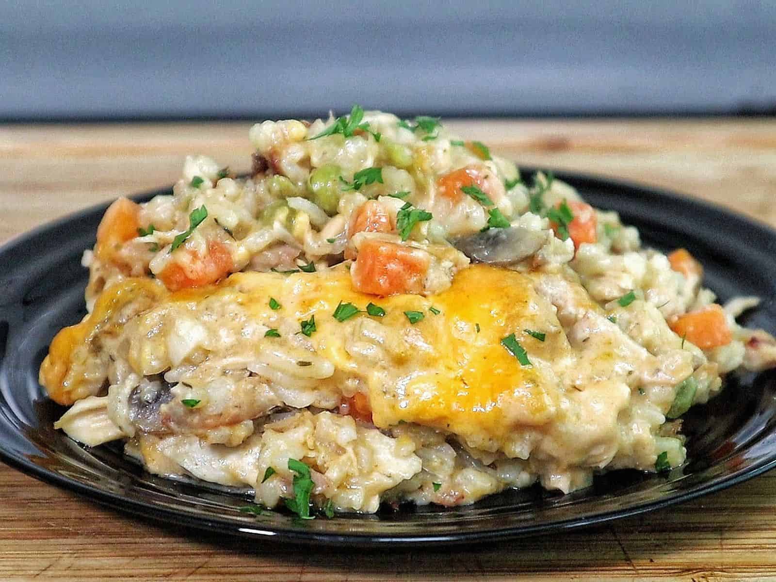 Creamy chicken and rice casserole topped with melted cheddar cheese, peas, carrots, and mushrooms with fresh parsley garnish.
