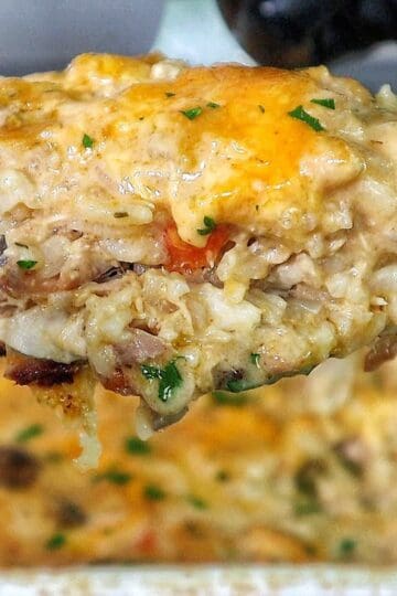 Creamy chicken and rice casserole topped with melted cheddar cheese, peas, carrots, and mushrooms with fresh parsley garnish.