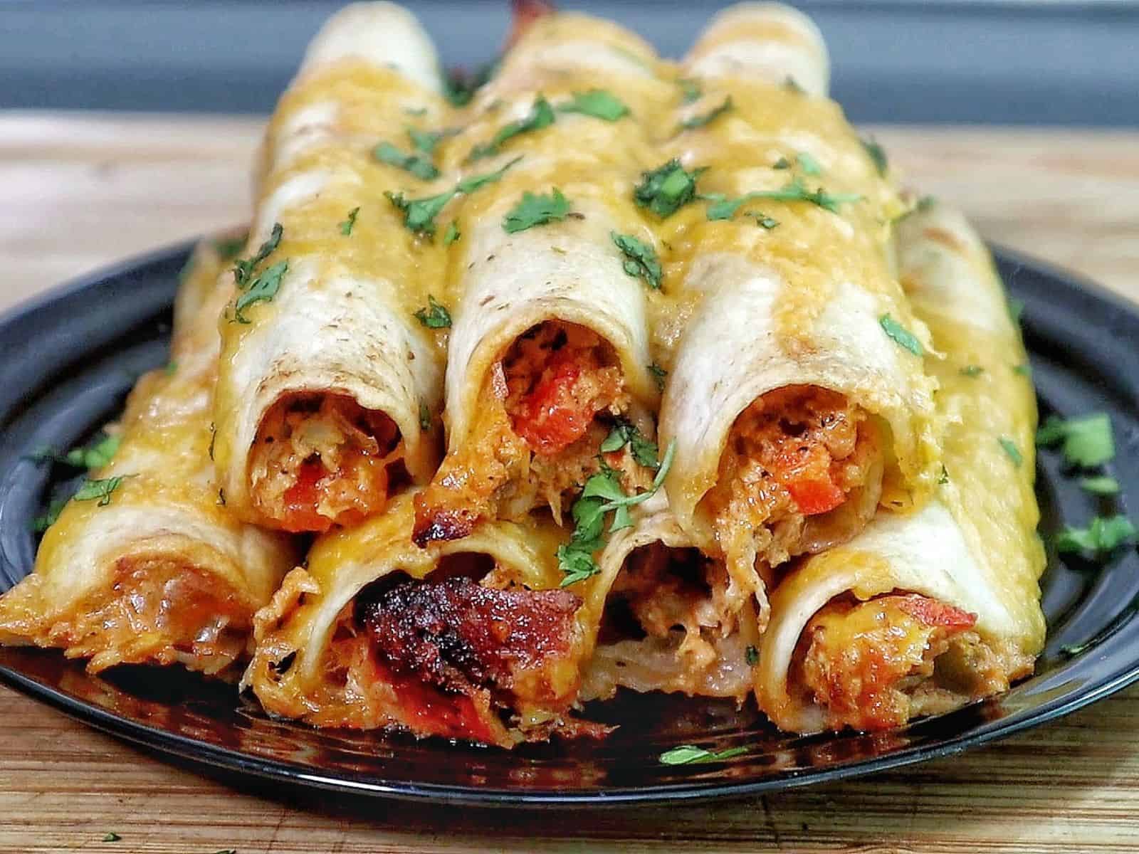 Golden brown crispy chicken taquitos filled with shredded chicken and red peppers, topped with melted cheese and fresh chopped cilantro.