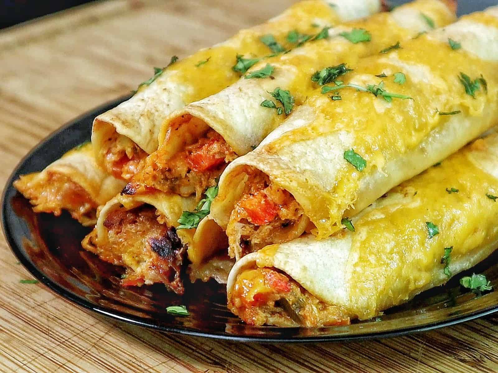 Golden brown crispy chicken taquitos filled with shredded chicken and red peppers, topped with melted cheese and fresh chopped cilantro.