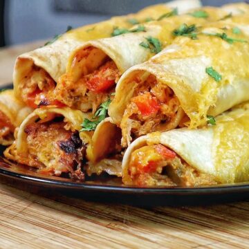 Golden brown crispy chicken taquitos filled with shredded chicken and red peppers, topped with melted cheese and fresh chopped cilantro.