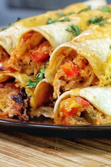 Golden brown crispy chicken taquitos filled with shredded chicken and red peppers, topped with melted cheese and fresh chopped cilantro.