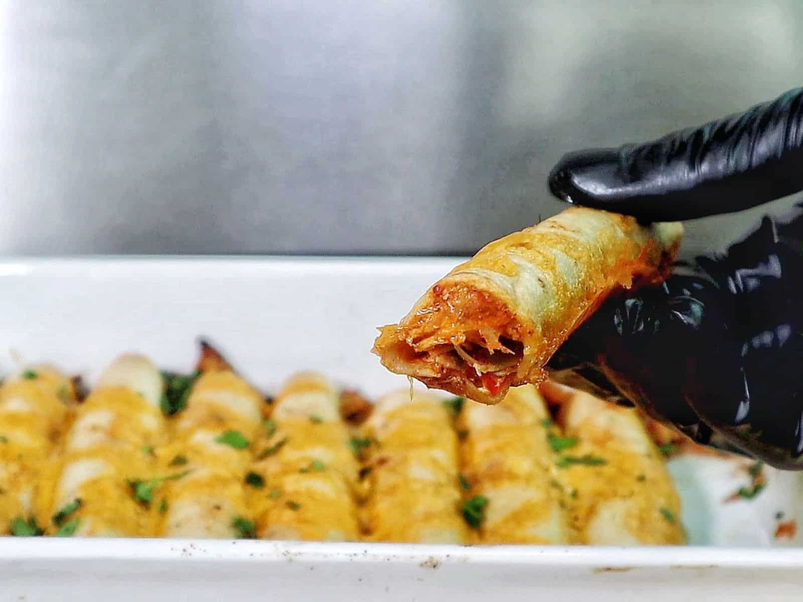 Golden brown crispy chicken taquitos filled with shredded chicken and red peppers, topped with melted cheese and fresh chopped cilantro.