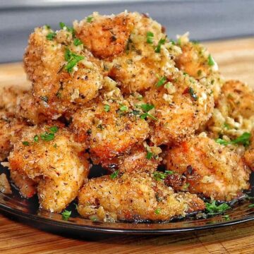 Golden brown garlic parmesan chicken bites piled on a black plate, coated in buttery garlic sauce and fresh parsley, with a crispy breadcrumb crust.
