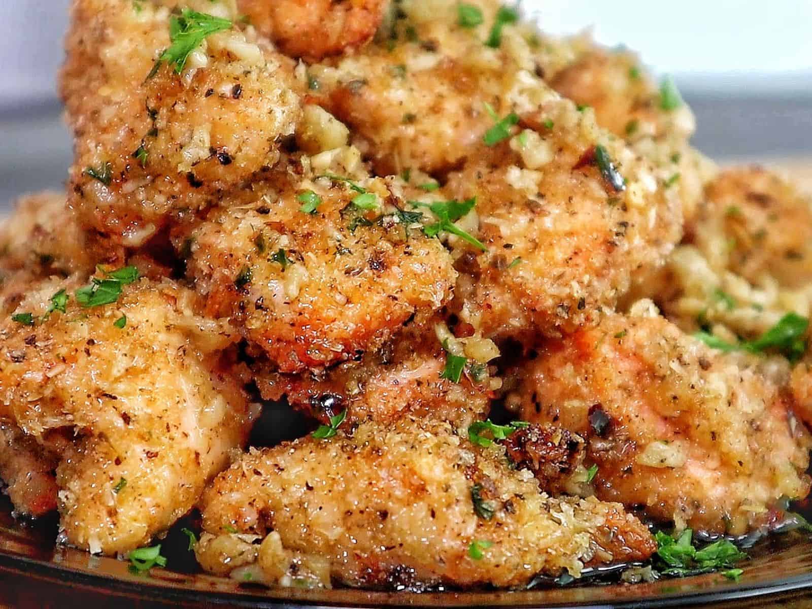 Golden brown garlic parmesan chicken bites piled on a black plate, coated in buttery garlic sauce and fresh parsley, with a crispy breadcrumb crust.