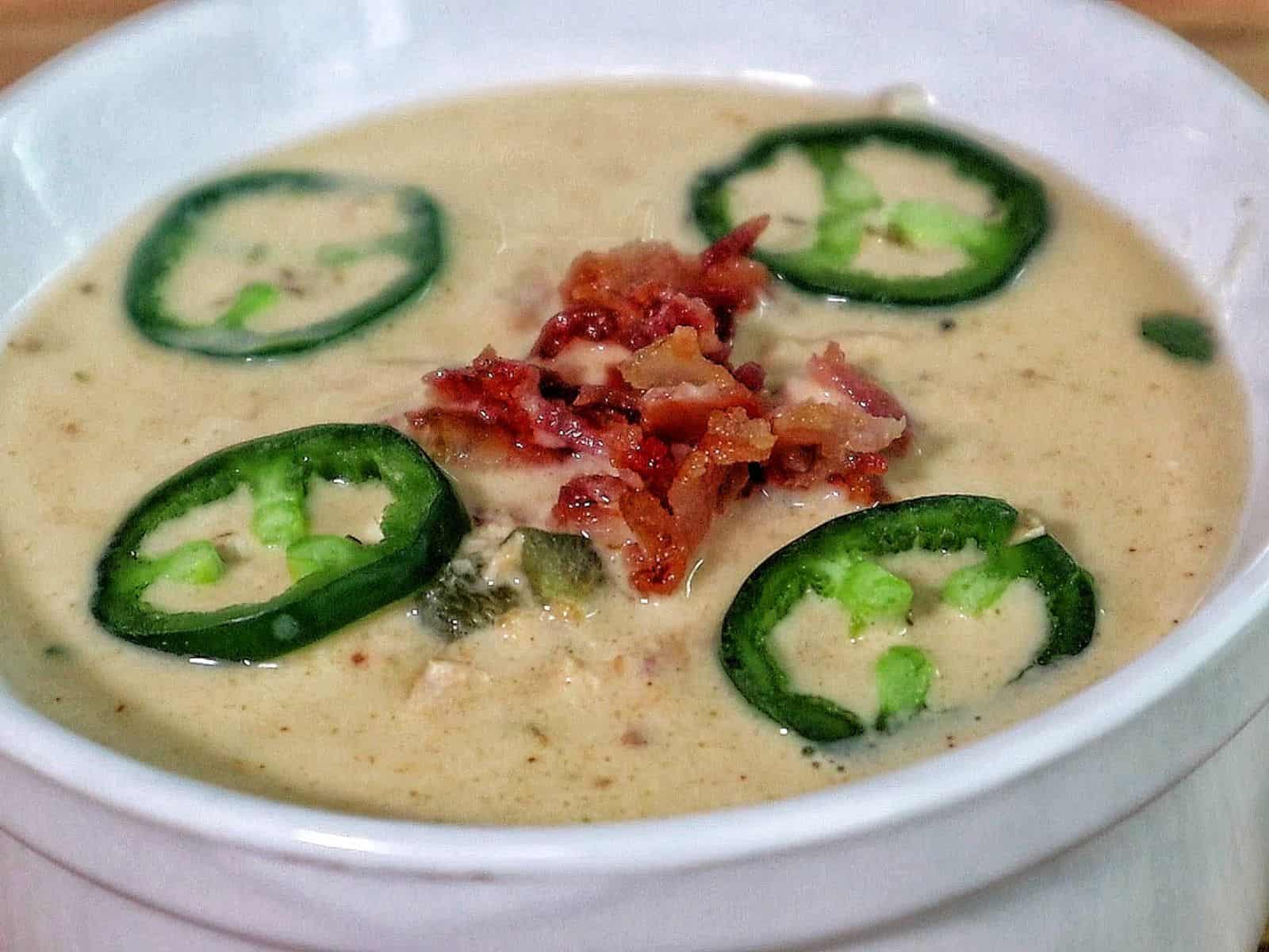 Creamy jalapeño popper chicken soup topped with fresh sliced jalapeños, crispy bacon, and chopped cilantro.