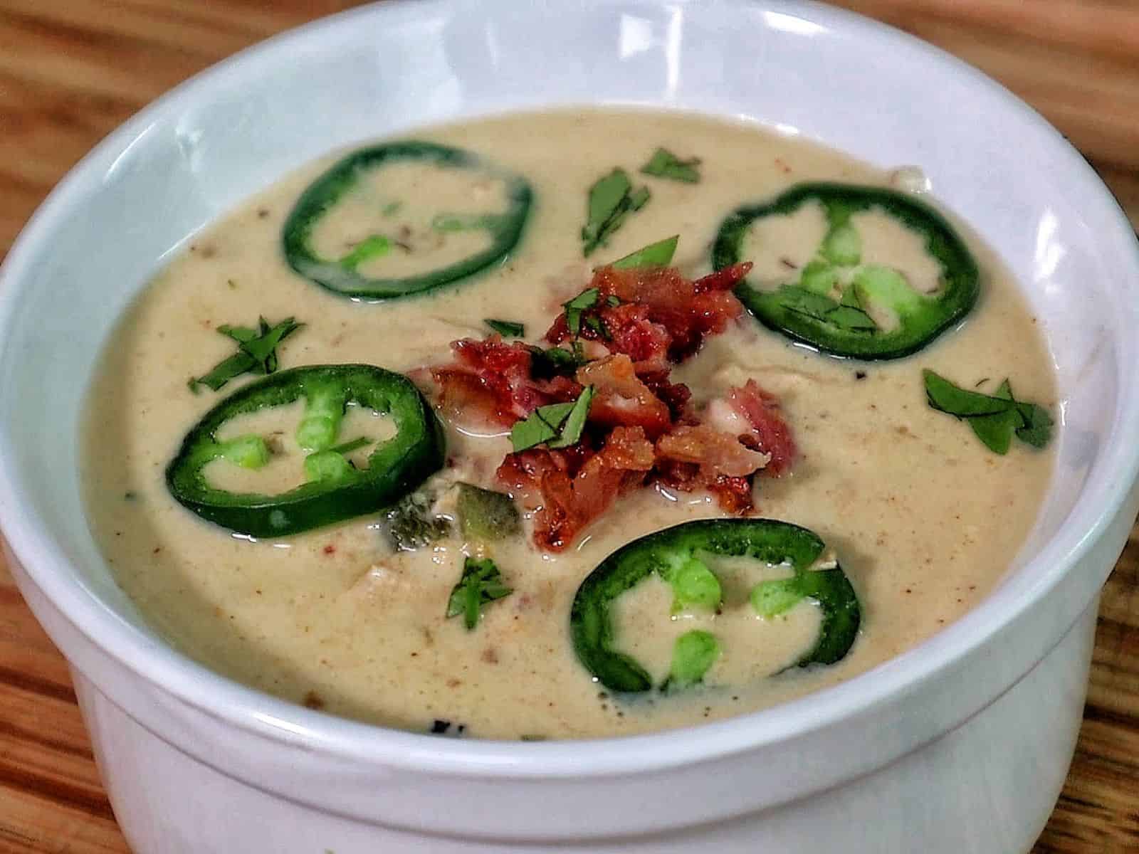 Creamy jalapeño popper chicken soup topped with fresh sliced jalapeños, crispy bacon, and chopped cilantro.