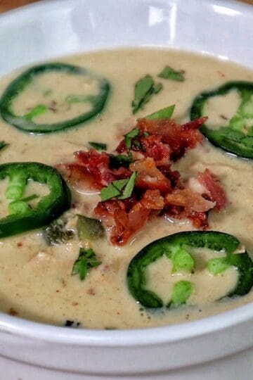 Creamy jalapeño popper chicken soup topped with fresh sliced jalapeños, crispy bacon, and chopped cilantro.