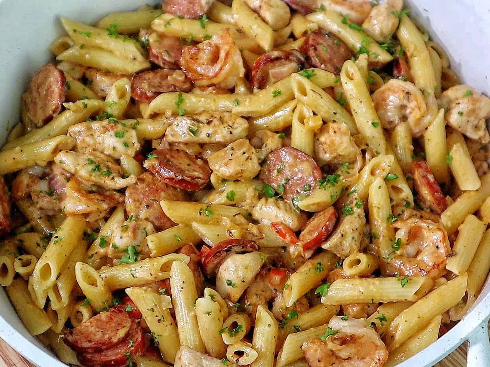 Creamy Cajun penne pasta with shrimp, sliced andouille sausage, and chunks of chicken, tossed in a rich Parmesan cream sauce and garnished with fresh parsley.