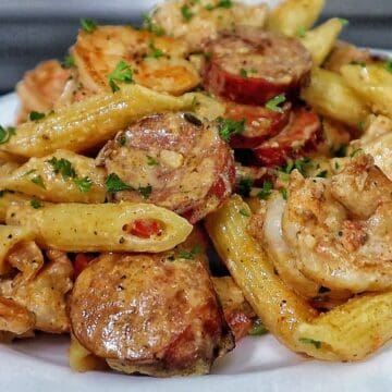 Creamy Cajun penne pasta with shrimp, sliced andouille sausage, and chunks of chicken, tossed in a rich Parmesan cream sauce and garnished with fresh parsley.