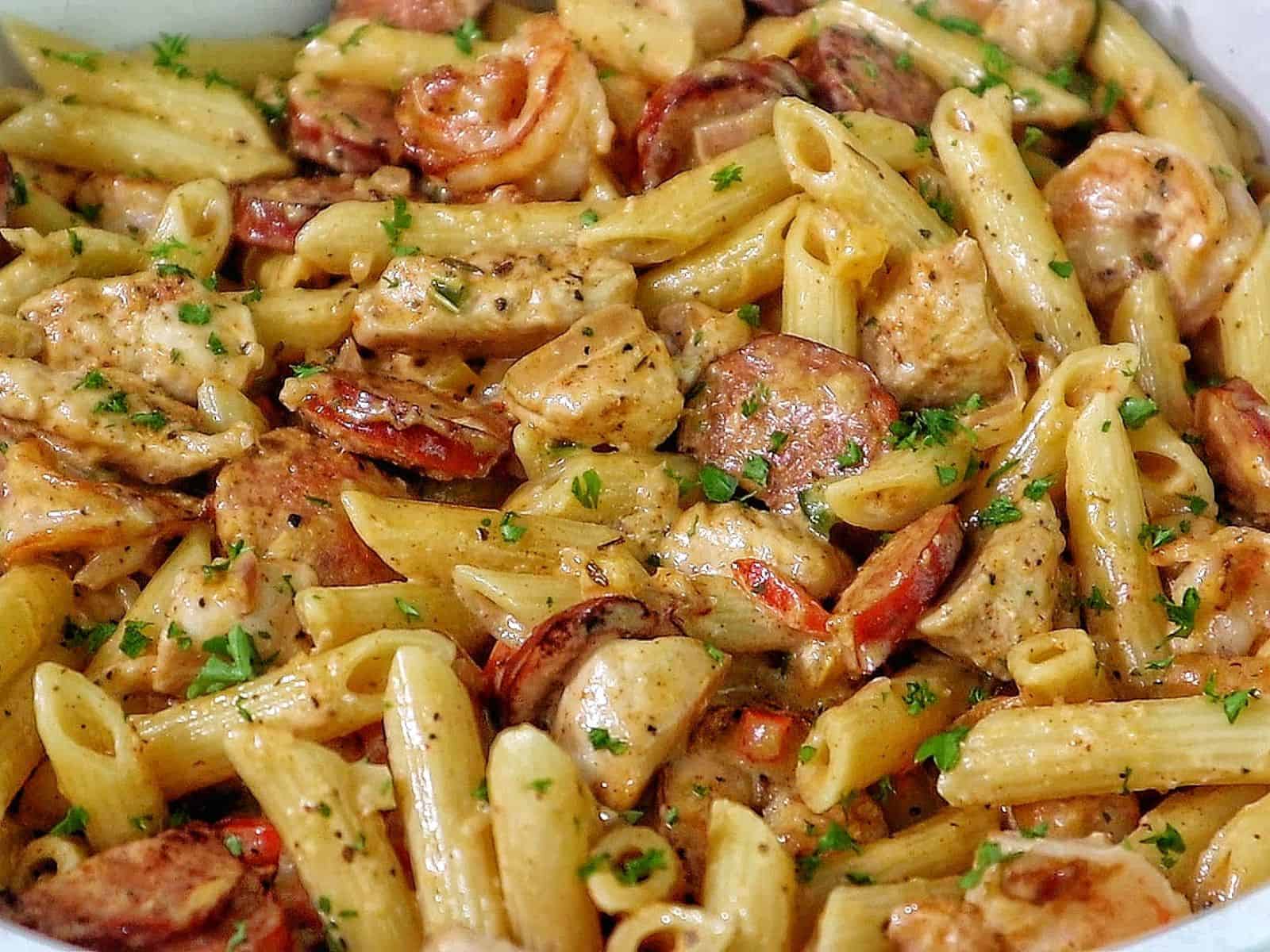 Creamy Cajun penne pasta with shrimp, sliced andouille sausage, and chunks of chicken, tossed in a rich Parmesan cream sauce and garnished with fresh parsley.