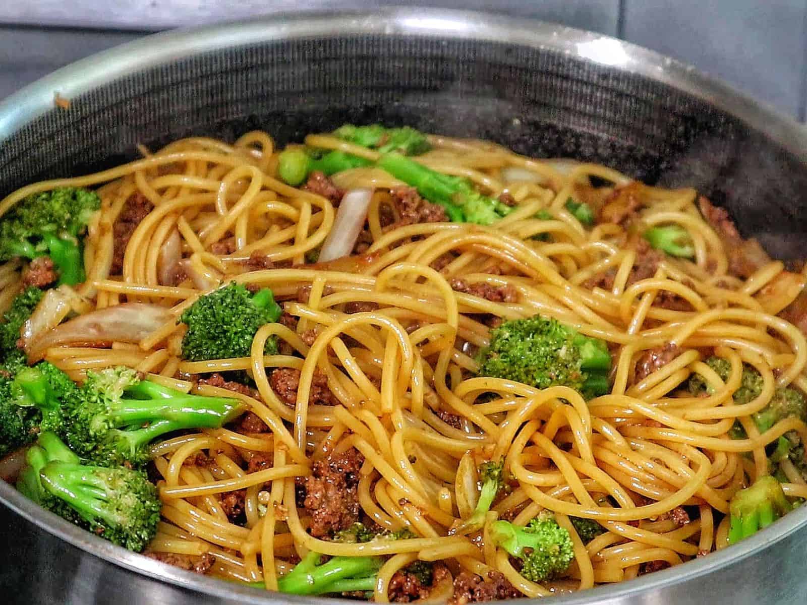 Beef stir-fried noodles with broccoli florets, red chili slices, and onions in a savory sauce.