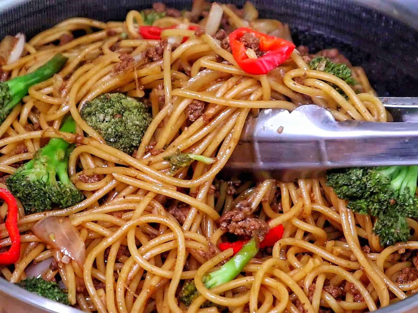 Beef stir-fried noodles with broccoli florets, red chili slices, and onions in a savory sauce.