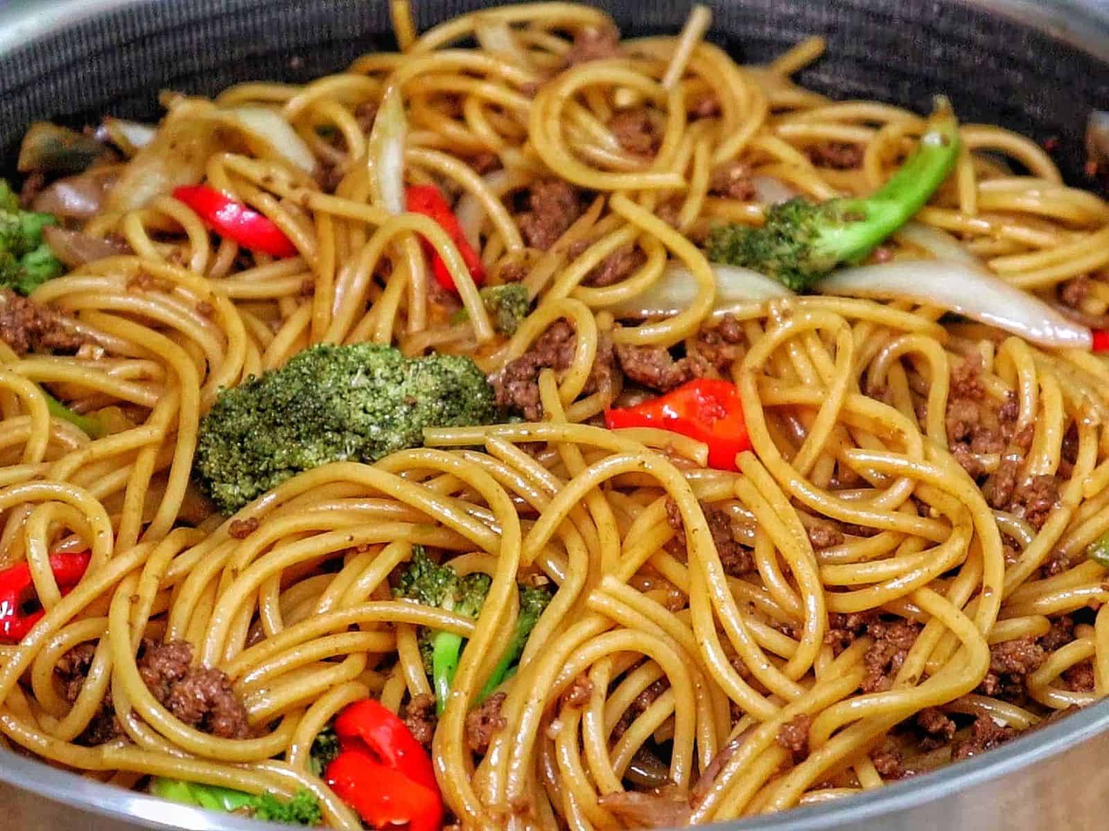Beef stir-fried noodles with broccoli florets, red chili slices, and onions in a savory sauce.