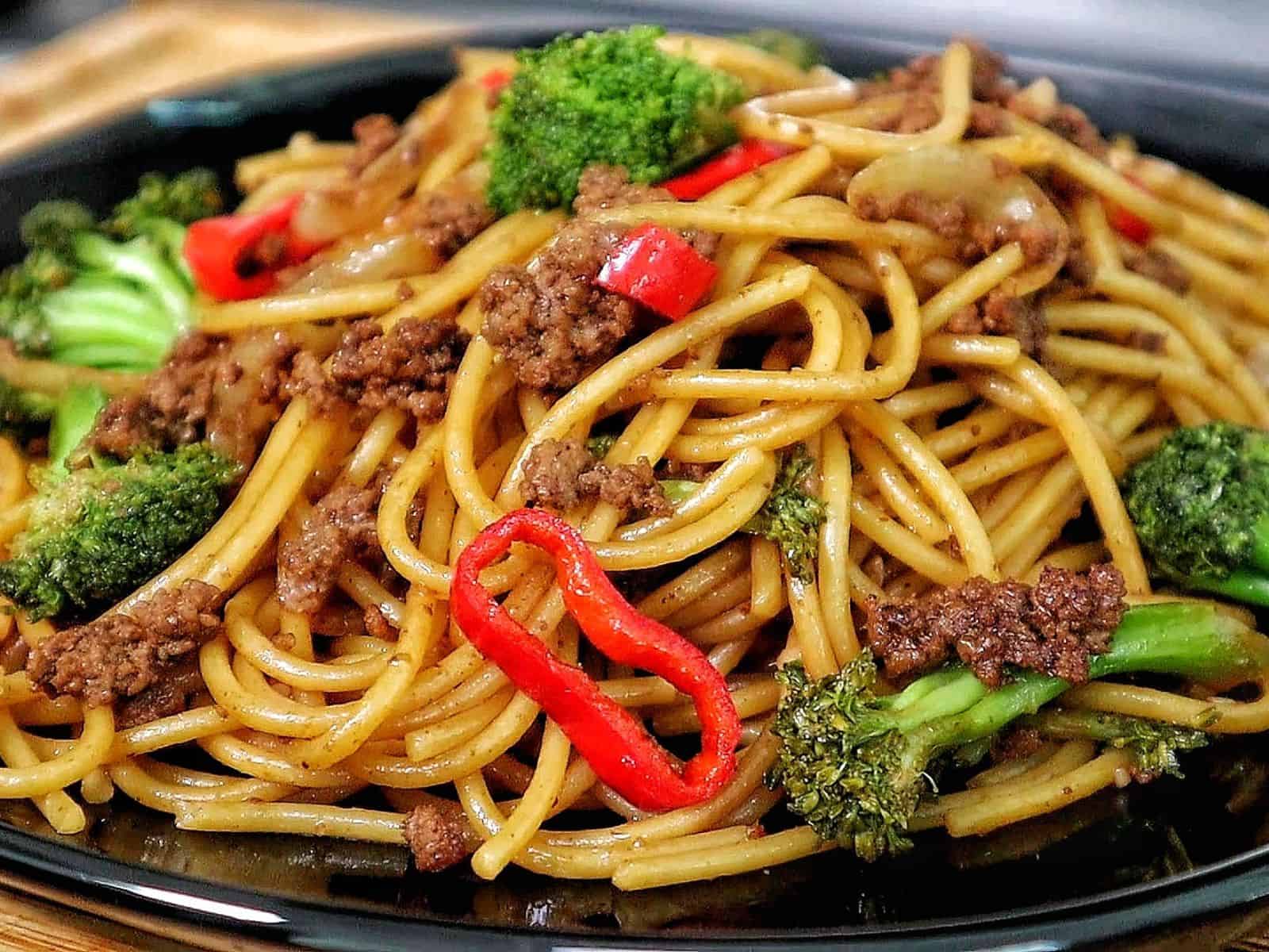 Beef stir-fried noodles with broccoli florets, red chili slices, and onions in a savory sauce.