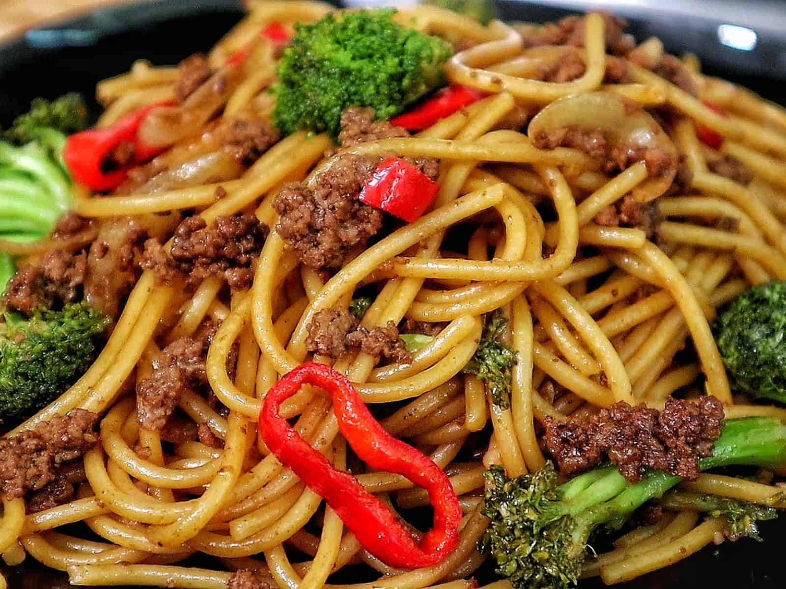Beef stir-fried noodles with broccoli florets, red chili slices, and onions in a savory sauce.