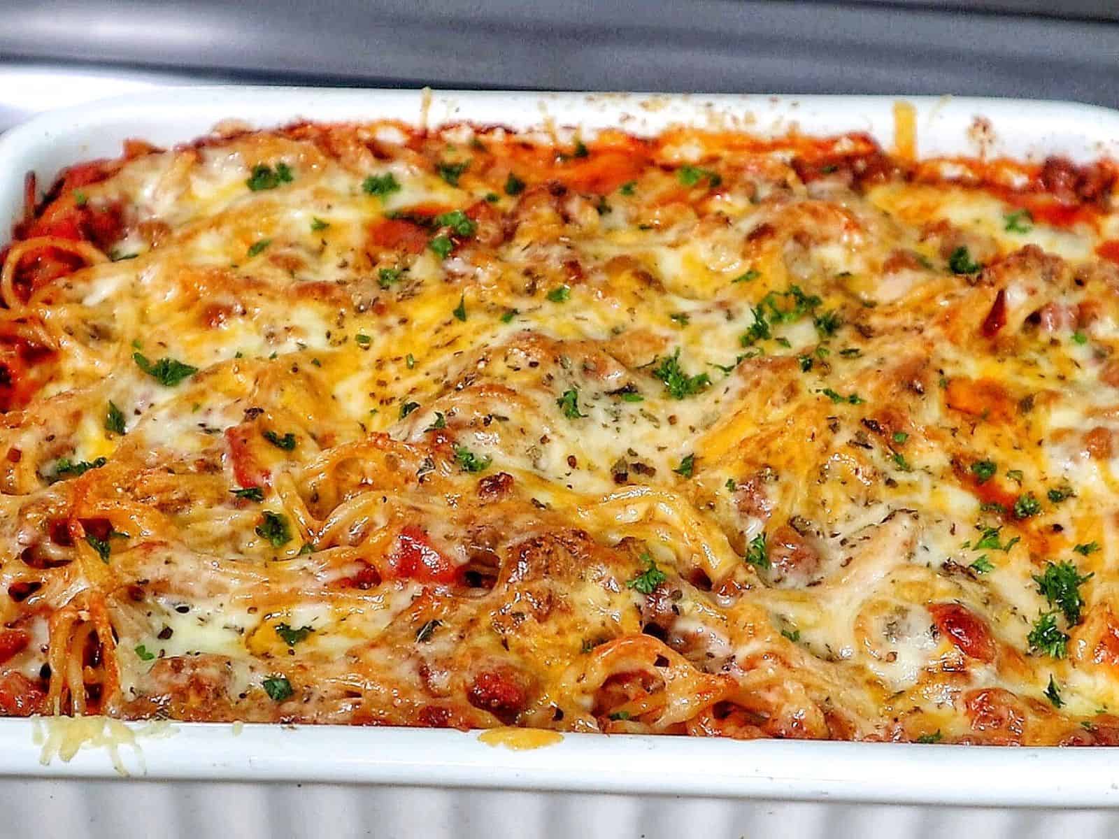 Cheesy baked spaghetti casserole with seasoned ground beef, tomato sauce, and melted mozzarella, cheddar, and parmesan.