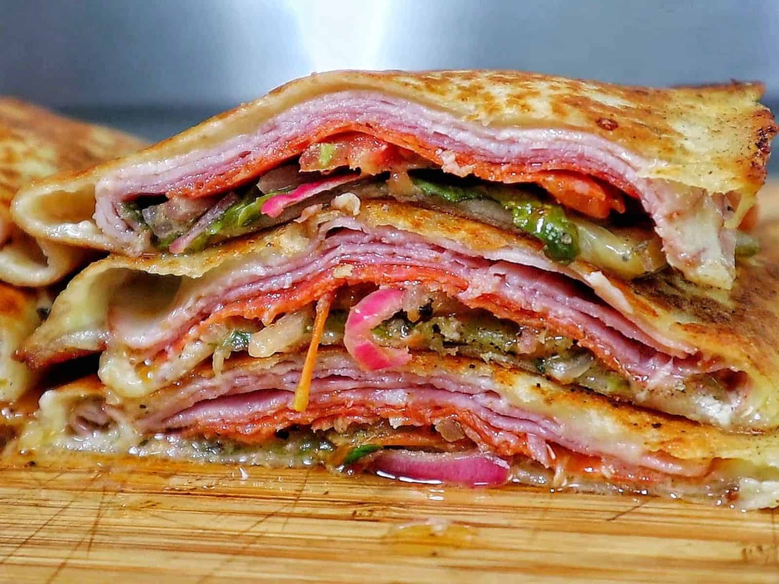 Toasted Italian sub wrap sliced in half, filled with layers of ham, salami, pepperoni, melted provolone cheese, lettuce, tomatoes, onions, and banana peppers.