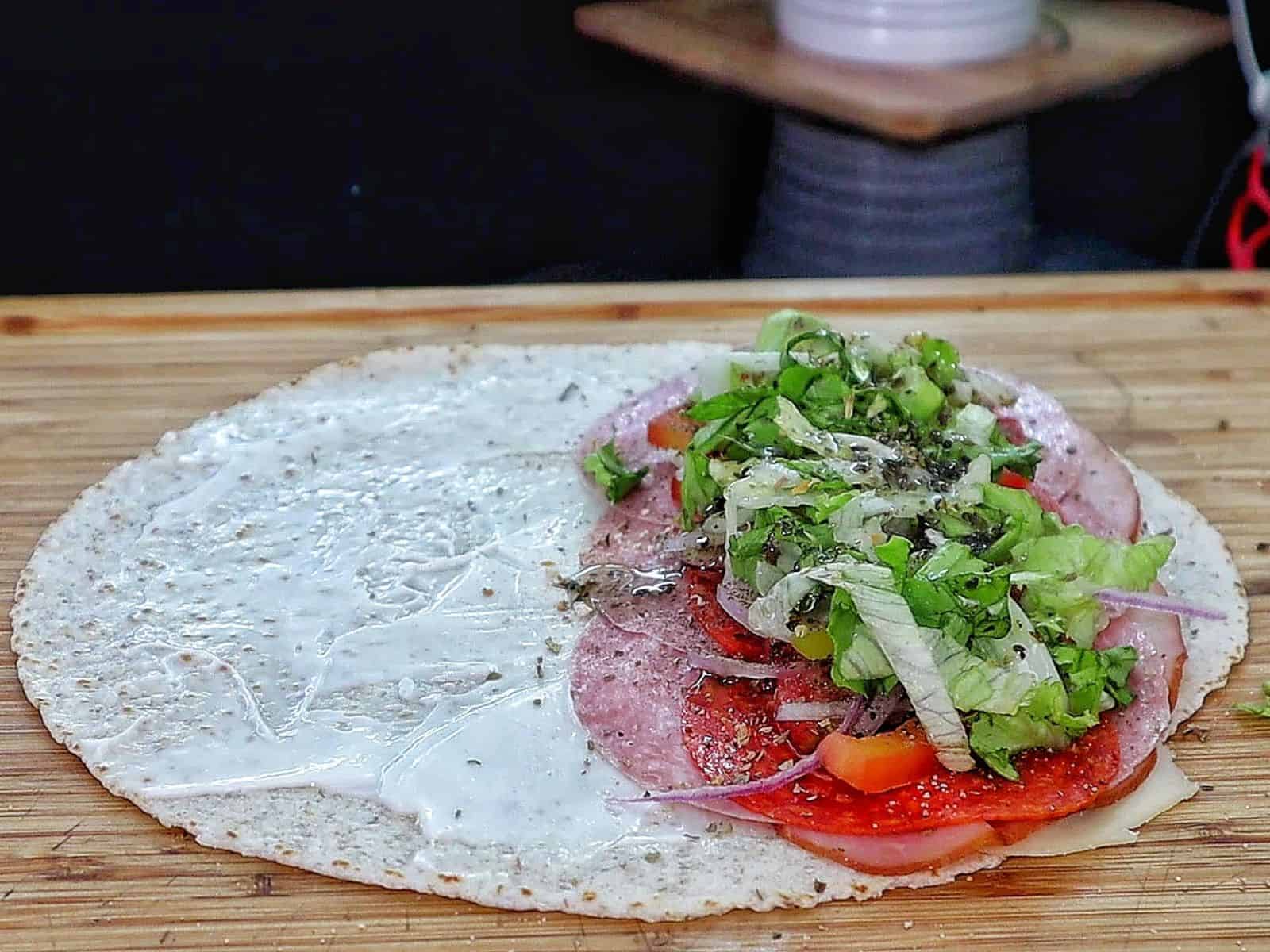 Toasted Italian sub wrap sliced in half, filled with layers of ham, salami, pepperoni, melted provolone cheese, lettuce, tomatoes, onions, and banana peppers.