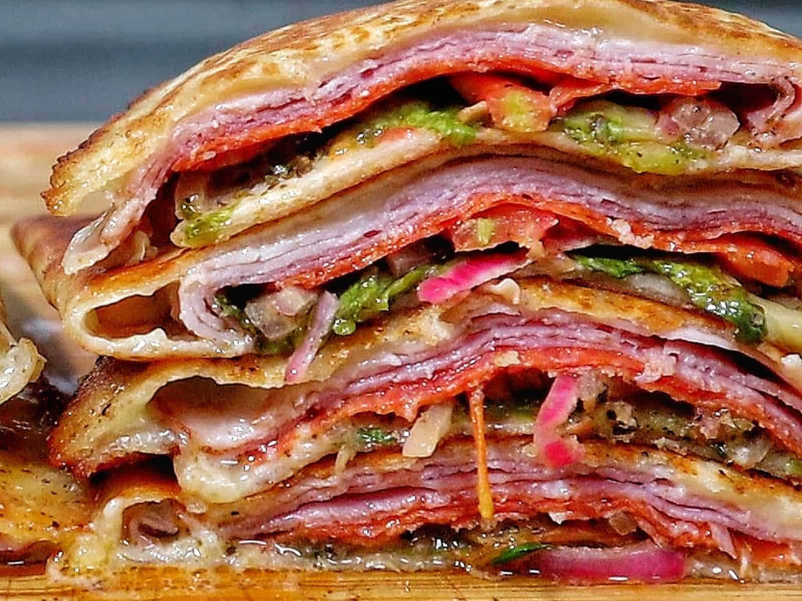 Toasted Italian sub wrap sliced in half, filled with layers of ham, salami, pepperoni, melted provolone cheese, lettuce, tomatoes, onions, and banana peppers.