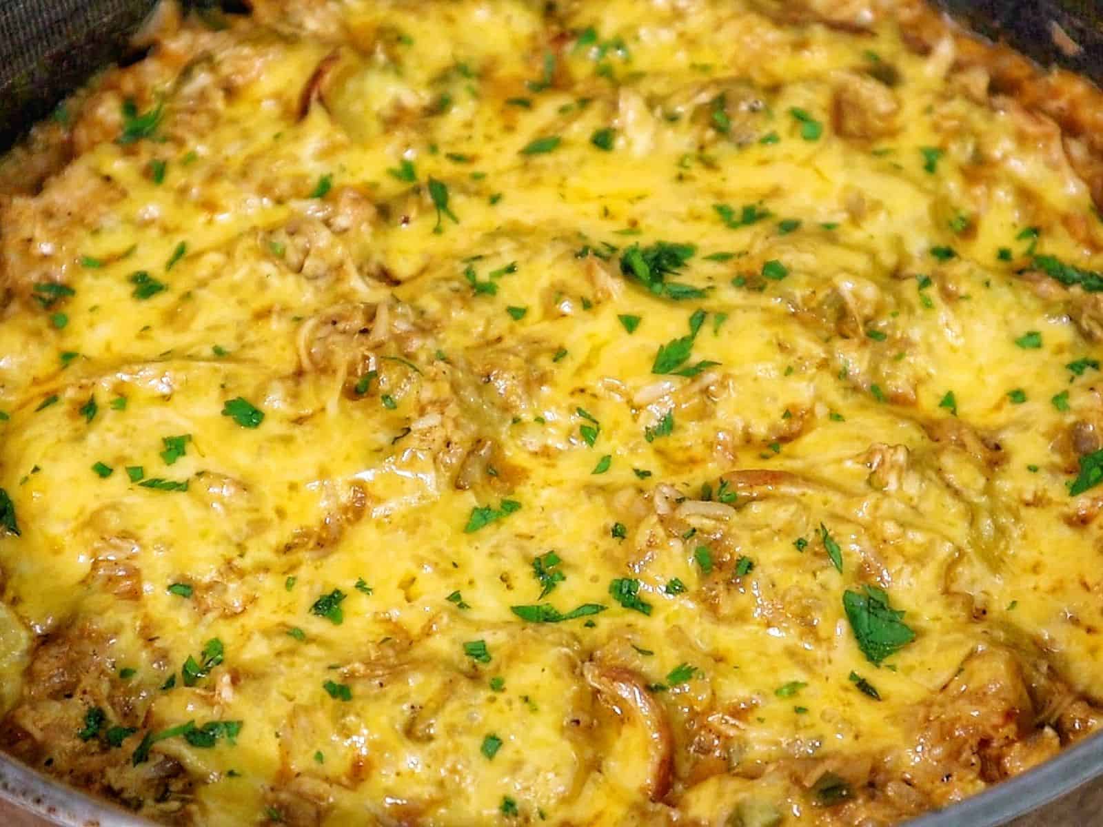 A skillet filled with cheesy buffalo chicken and rice, topped with melted cheddar cheese and herbs.