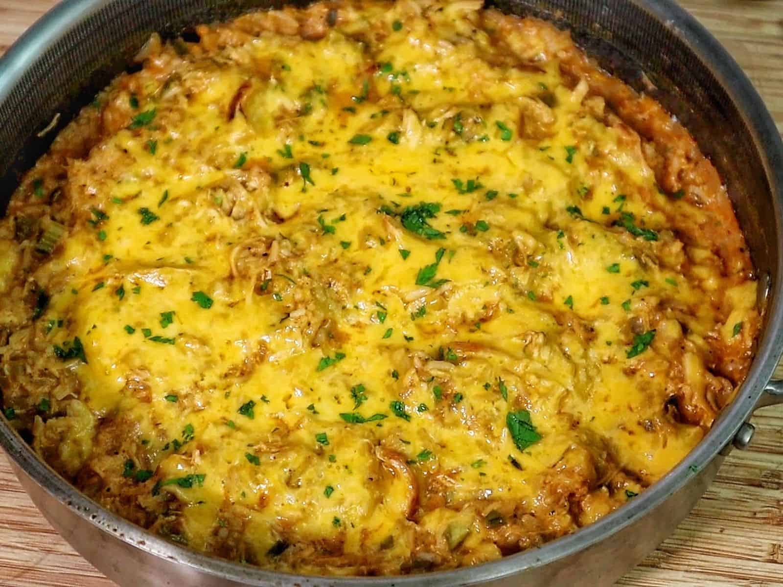 A skillet filled with cheesy buffalo chicken and rice, topped with melted cheddar cheese and herbs.