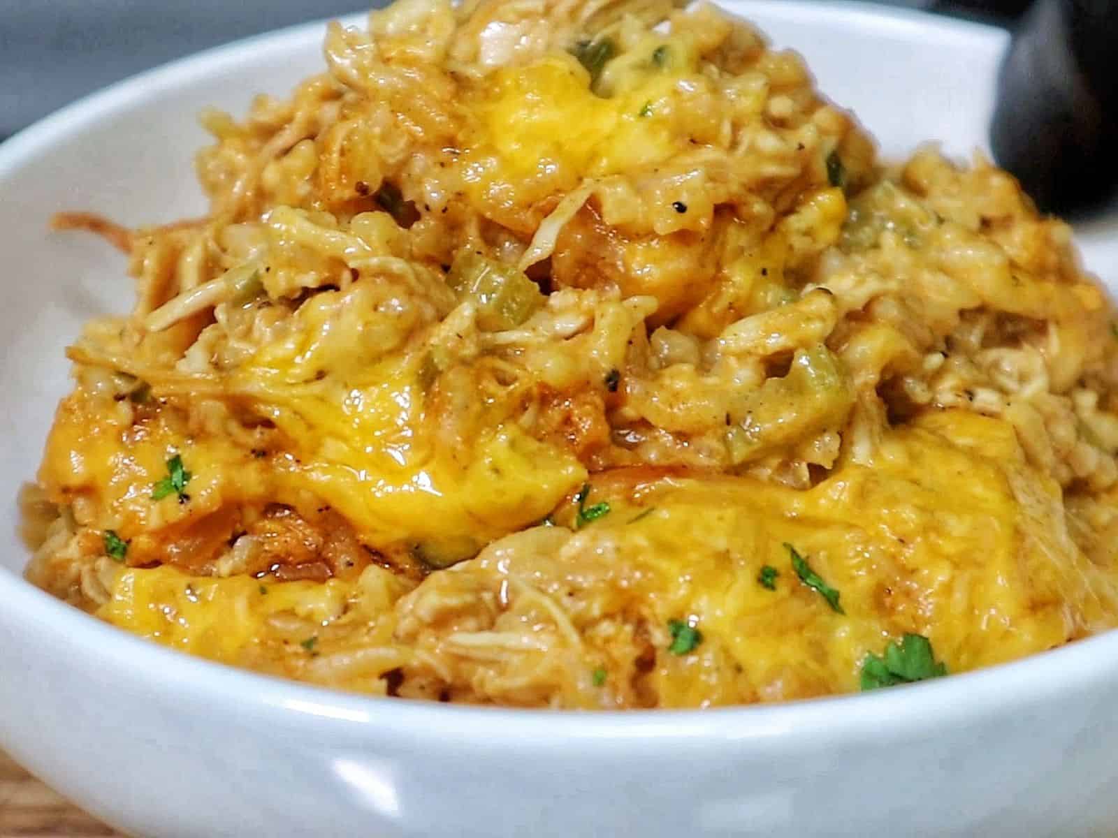 A skillet filled with cheesy buffalo chicken and rice, topped with melted cheddar cheese and herbs.