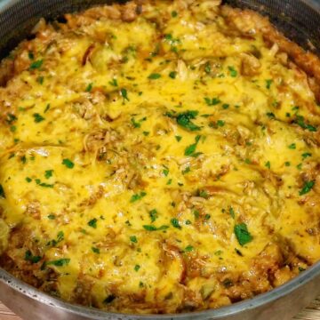 A skillet filled with cheesy buffalo chicken and rice, topped with melted cheddar cheese and herbs.